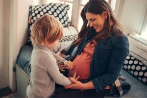Pregnant mother smiling and holding her young child at home, representing surrogacy and family connection.